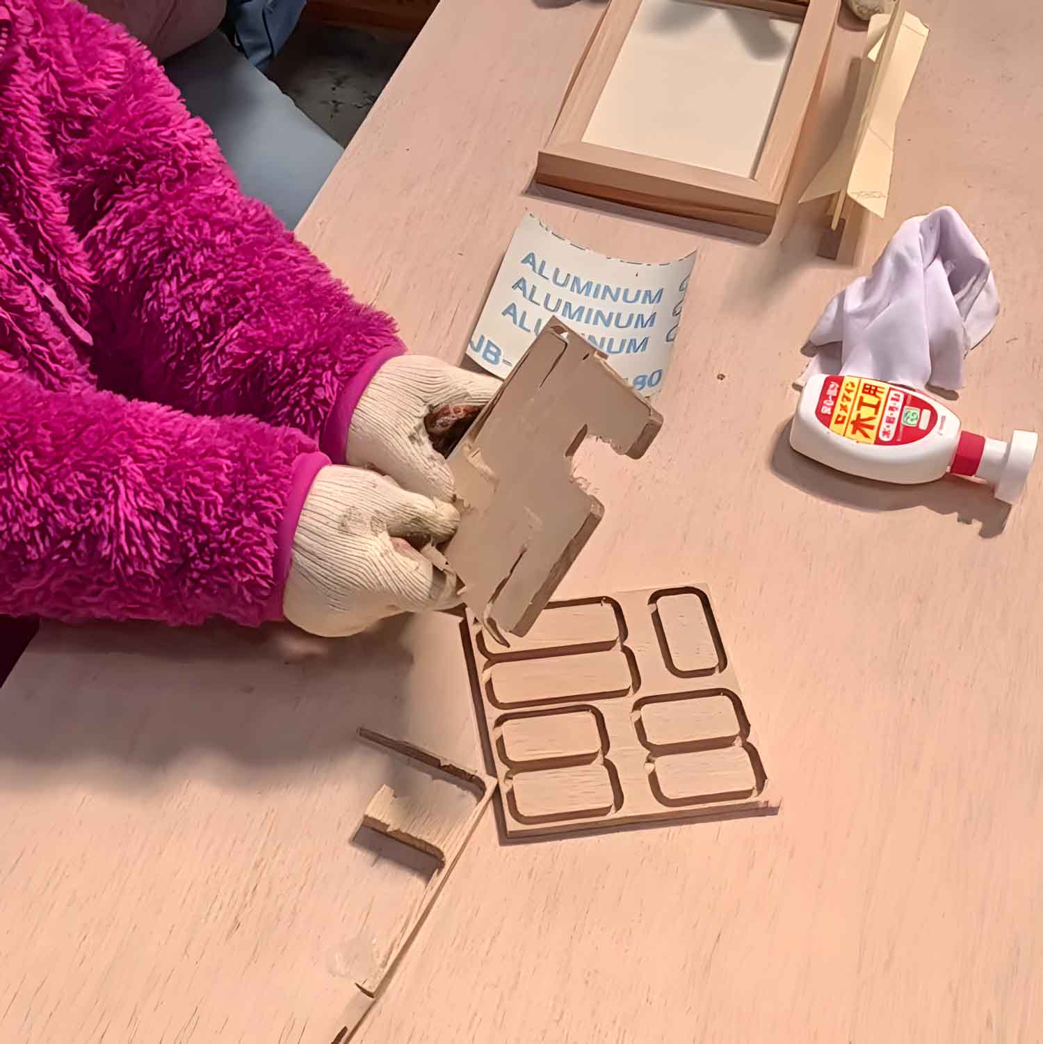 Scene from a woodworking event. Small children are assembling wooden parts by hand together with adults, grandfathers, and grandmothers. Toys made from natural materials that are safe for children to play with. SOZOZAKKA. そうぞうざっか.